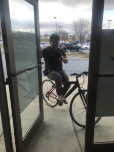 man on a bicycle holding open the front door of the V Eye P Frederick location